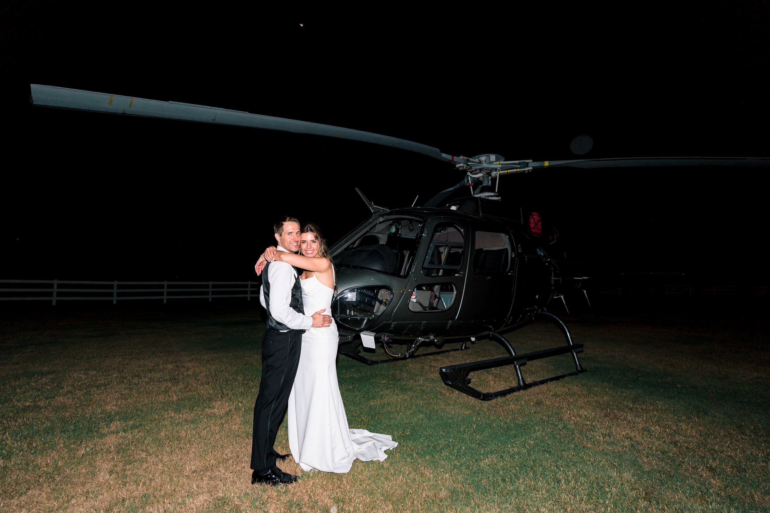 Bride and groom embracing in front of a helicopter at night